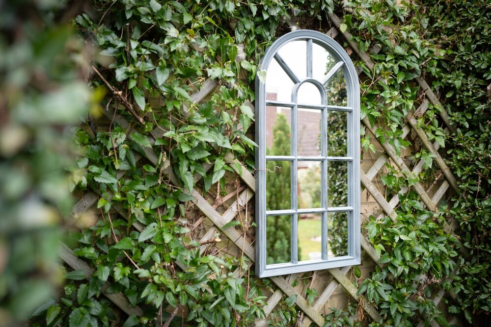 Shallow focus of a vertical garden showing a ornate mirror seen attached to a trellis with vines growing around the frame.